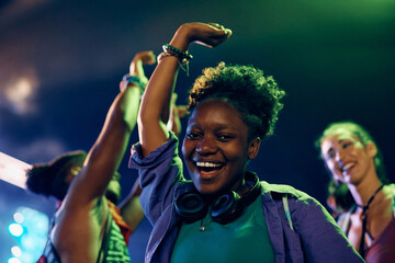 Happy black woman having fun and dancing on open air music concert at night.
