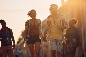 Young carefree couple going with friends on music festival at sunset.