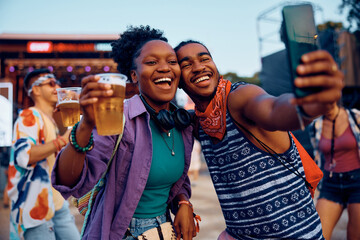 Cheerful black couple taking selfie on summer music festival.