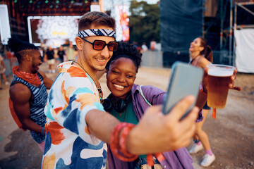 Happy couple having fun and taking selfie during music concert in summer.