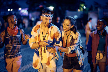 Happy couple using cell phone on summer music concert at night. - obrazy, fototapety, plakaty
