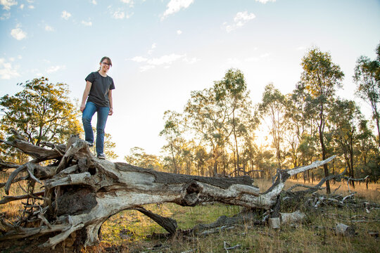Happy teen girl walking along a fallen tree stump in paddock