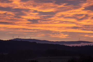Wind turbines are in the background mountains in a foggy sunrise