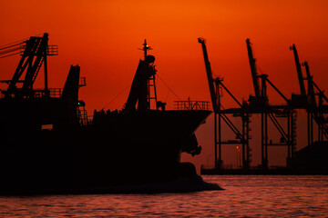 Obraz premium 関門海峡の朝焼けの中のガントリークレーンと貨物船のシルエット20240218-2