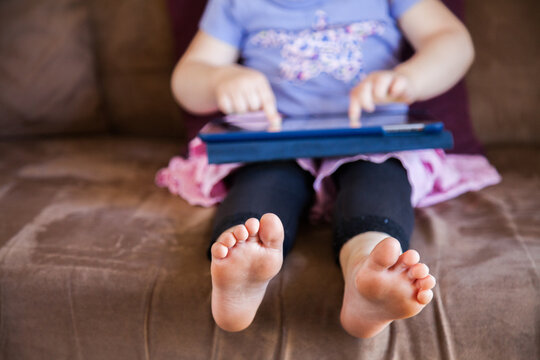 Three year old child playing game on ipad on lounge