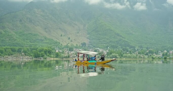 Traditional Shikara boat sailing on the calm waters of Dal Lake in Srinagar, Kashmir, India, with lush green mountains, reflections, and a serene Himalayan landscape.