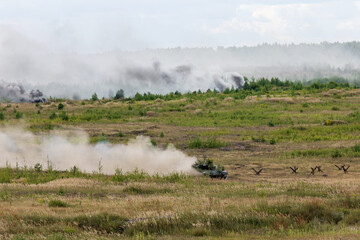 Fototapeta na wymiar Heavy combat vehicles tanks drive around the butts and put up a smoke screen