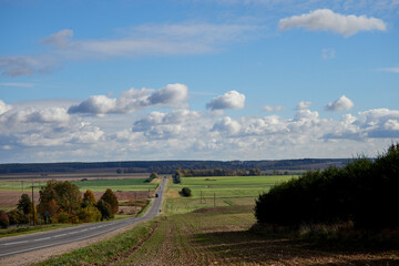 Asphalt road, field and forest with sky and clouds. Landscape of the Central Russian plain in early autumn