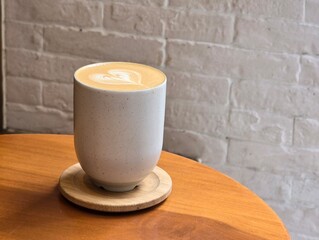 Latte coffee in classic no handle cup with white vintage bricks background and wooden table - 744436805