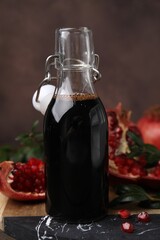 Tasty pomegranate sauce in bottle, fruits and branches on table, closeup