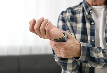 Arthritis symptoms. Man suffering from pain in wrist at home, closeup. Space for text