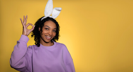 Easter studio shot with cute young woman in easter bunny ears showing ok sign. Copy space banner