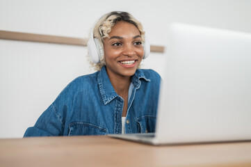 smiling african american woman sitting at desk, using laptop taking notes, watching tutorial,...