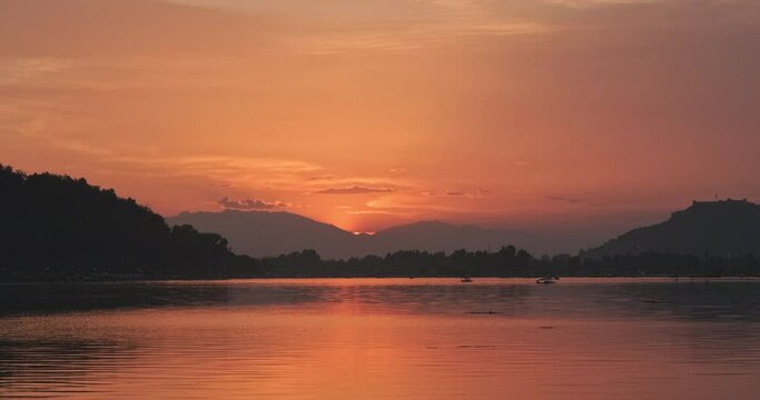 Dal Lake Kashmir, India looks red after the sunset. the boats passing through creating a reflection on the water. The sunset creates a hue in the sky and the clouds are illuminated with the backlight.