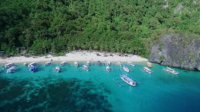 Seven Commandos Beach in Palawan, Sightseeing Place. Tour A in El Nido, Philippines. Serene white sand beach with clear turquoise water, palm trees  rock formations in Background. Drone