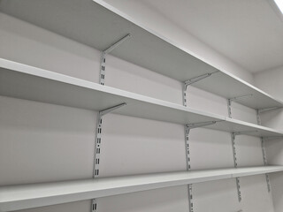 empty white room with gray carpet and shelves along entire wall. metal holders and laminate shelves...