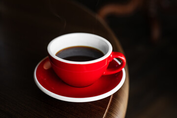 A red cup of black coffee on a saucer on the edge of wooden table, copy space - 744463253