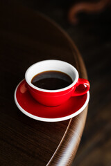 A red cup of black coffee on a saucer on the edge of wooden table, copy space - 744463608