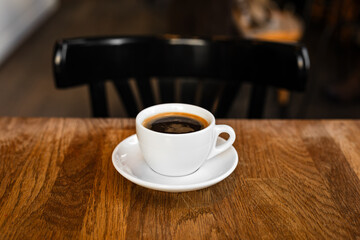A white cup of black coffee on a saucer on the wooden table in a cafe - 744464866