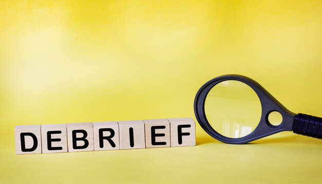 Wooden cubes with debrief text on a yellow background next to a magnifying glass