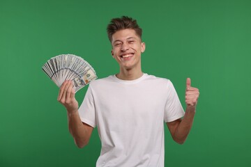 Happy man with dollar banknotes showing thumb up on green background