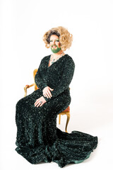 Smiling Drag Queen in Sparkling Black Gown Seated Elegantly on Gold Chair