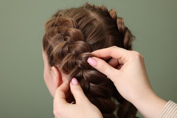 Fototapeta premium Professional stylist braiding woman's hair on olive background, closeup
