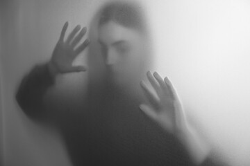 Silhouette of ghost behind fabric against light grey background. Black and white effect