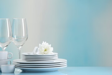 Set of many clean dishware, flower and glasses on light blue table. Space for text