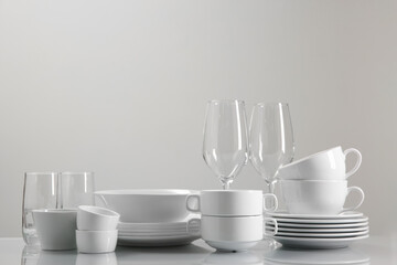 Set of many clean dishware and glasses on light table. Space for text