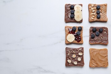Different tasty toasts with nut butter and products on white marble table, flat lay. Space for text