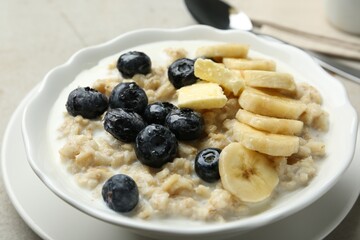 Tasty oatmeal with banana, blueberries, butter and milk served in bowl on light grey table, closeup
