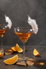 Tasty cocktails in glasses decorated with cotton candy and orange slices on gray table