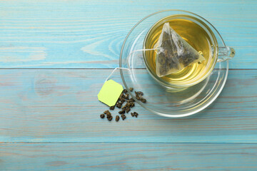 Tea bag in cup with hot drink and dry leaves on light blue wooden table, top view. Space for text