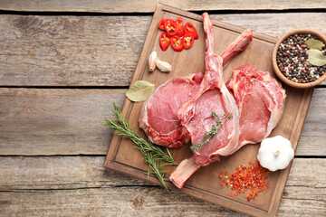 Fresh tomahawk beef cuts and spices on wooden table, top view. Space for text