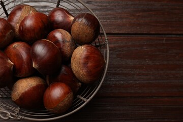 Sweet fresh edible chestnuts in metal basket on wooden table, top view. Space for text