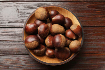 Obraz premium Sweet fresh edible chestnuts in bowl on wooden table, top view