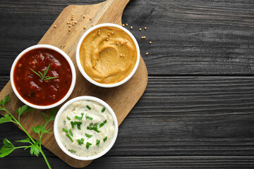 Different tasty sauces in bowls and parsley on black wooden table, top view. Space for text