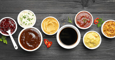 Different tasty sauces in bowls, parsley, chili pepper and rosemary on black wooden table, flat lay