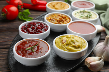 Different tasty sauces in bowls and garlic on wooden table, closeup