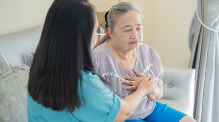 Fototapeta premium Sick older woman with chest pain touching inflammated zone and middle-aged woman or nurse take care of her.