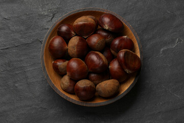 Roasted edible sweet chestnuts in bowl on grey textured table, top view