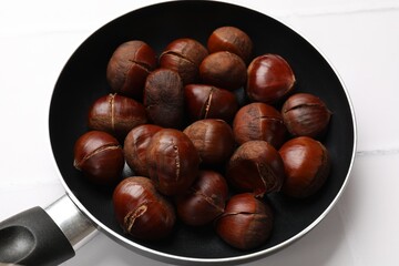 Fresh edible sweet chestnuts in frying pan on white tiled table, closeup