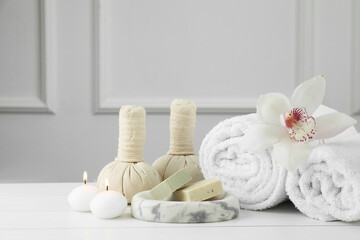Beautiful spa composition. Towels, herbal bags, soap bars and burning candles on white wooden table, space for text