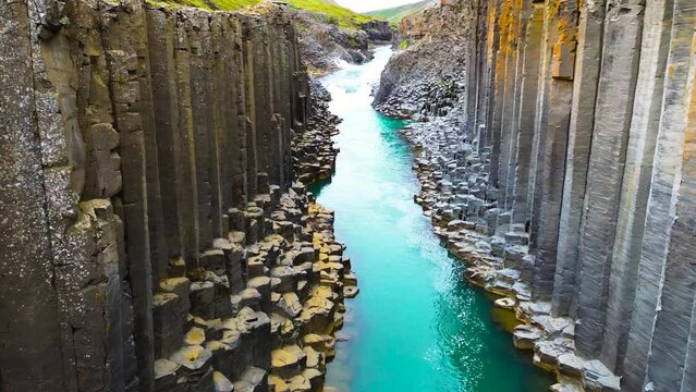 Flying through the Studlagil Canyon with the Jokulsa. Bru river in east Iceland, basalt rocks, Europe. Studlagil basalt rock columns canyon area and a stunning blue-green glacial river.