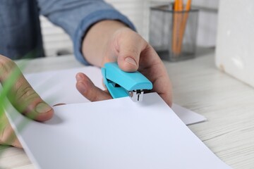 Man with papers using stapler at white wooden table indoors, closeup