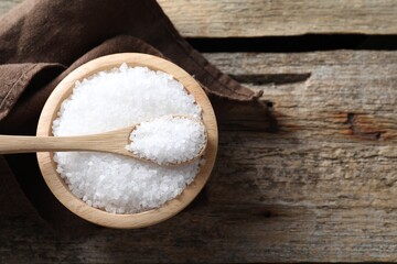 Organic salt in bowl and spoon on wooden table, top view. Space for text