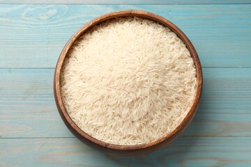 Raw basmati rice in bowl on light blue wooden table, top view
