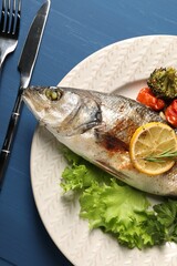 Delicious baked fish and vegetables served on blue wooden table, top view