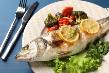 Delicious baked fish and vegetables served on blue wooden table, closeup